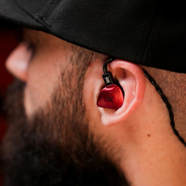 Primer plano de una oreja con auricular rojo puesto, cable por encima y gorra negra