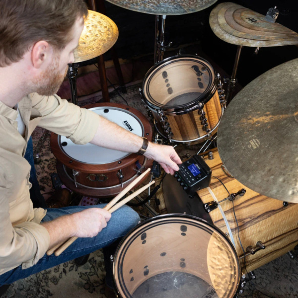 Músico tocando una batería acústica con el KitStream fijado en el aro del bombo.